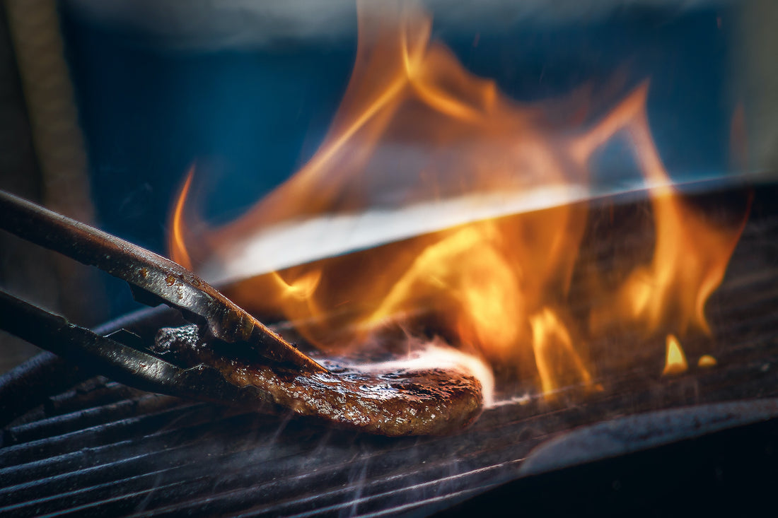 Grilling steak on a charcoal griller with a pair of tongs
